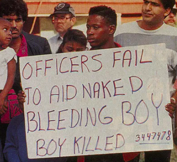 Caso Dahmer, manifestanti con cartello "Officers fail to aid naked bleeding boy. Boy killed"